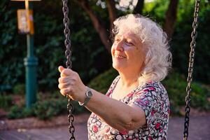 An elderly lady in the park is holding on to the chain of a swing. photo