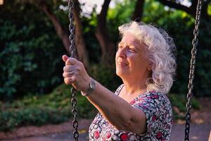 An elderly lady in the park is holding on to the chain of a swing. photo