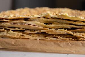 Backing process. Closeup of Puff pastry layers of the delicious French Napoleon cake laying on the backing paper. French pastry with custard butter cream. Side view. Selective focus. photo