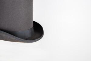 Magic hat. Topper. Elegant vintage gray beige wool felt top hat with black band on the wooden hat block. Grosgrain ribbon trim around rolled brim. Isolated on white background. Close-up. Copy space. photo
