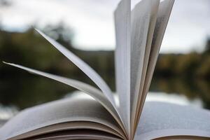 Pages of an open book on the wooden deck on the lake in the forest. Concept of reading, relaxing, meditating, education, visiting libraries, book exhibitions. Close up. Side view. Selective focus photo