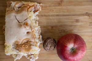 Piece of traditional thanksgiving apple cinnamon pie, apples and walnuts on the wooden cutting board on the white table. Homemade baked fruit tart with crust. Close up, copy space. Selective focus photo
