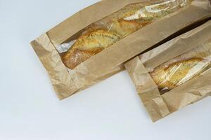 Closeup of two french baguettes in the brown kraft paper plastic bag isolated on white background. Fresh baked bread for sell. High resolution studio photo. Minimalist design. Top view. Copy space. photo