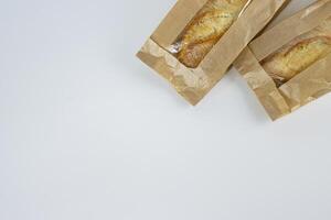 Closeup of two french baguettes in the brown kraft paper plastic bag isolated on white background. Fresh baked bread for sell. High resolution studio photo. Minimalist design. Top view. Copy space. photo