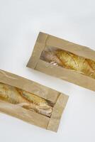 Closeup of two french baguettes in the brown kraft paper plastic bag isolated on white background. Fresh baked bread for sell. High resolution studio photo. Minimalist design. Top view. Copy space. photo