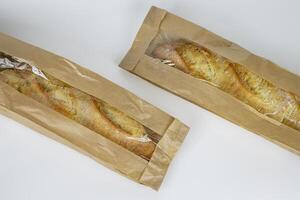 Closeup of two french baguettes in the brown kraft paper plastic bag isolated on white background. Fresh baked bread for sell. High resolution studio photo. Minimalist design. Top view. Copy space. photo