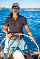 Young man captain stands at the helm and controls a sailboat during a journey by sea. High quality photo