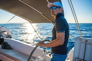 Young man captain stands at the helm and controls a sailboat during a journey by sea. High quality photo