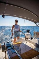 Young woman female captain stands at the helm and controls a sailboat during a journey by sea. High quality photo