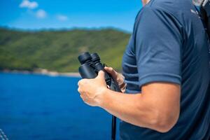 Young man captain on the yacht looking through binoculars during sailing boat. Travel and active life. Yachting. High quality photo