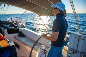 Young man captain stands at the helm and controls a sailboat during a journey by sea. High quality photo