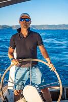 Young man captain stands at the helm and controls a sailboat during a journey by sea. High quality photo