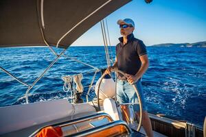 Young man captain stands at the helm and controls a sailboat during a journey by sea. High quality photo