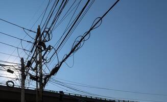 Intricate Network of Power Lines Against a Clear Blue Sky with Overpass in Background photo