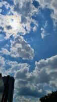 Angled view of a large, window covered building corner against a blue, cloud filled sky photo