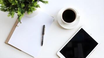 Flat lay showcasing tablet computer laid out next to a notepad with pen and coffee cup decorate by green little tree. top view of office accessories on working desk minimal scene photo