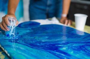Person creating blue acrylic pour art on canvas. Art and creativity concept. photo