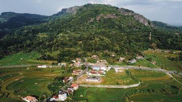 Panorama of the Nglanggeran Ancient Volcano ecotourism area in the afternoon using a drone. Aerial photo of an ancient stone hill covered with lush trees and surrounded by rice fields and countryside