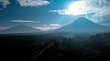 Landscape of Mount Merapi from a distance of 7 km before midday and the sun is directly behind the mountains. Aerial panorama of Mount Merapi during the day with white clouds around it photo