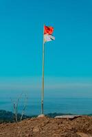 The peak of the ancient volcano Nglanggeran is dominated by rocks and contains the red and white Indonesian flag. Photo of rocky mountain peak with waving flag on a tropical morning