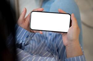 A close-up image of a woman holding a smartphone with a white-screen mockup in a horizontal position photo