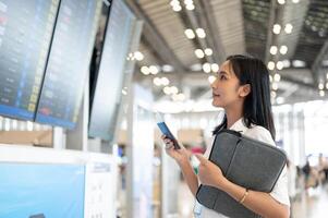 A beautiful Asian woman with her passport is standing in front of a flight information display. photo