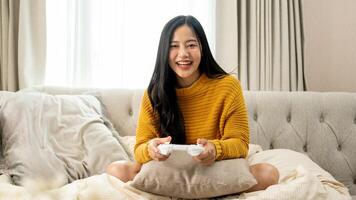 An attractive, fun Asian woman is enjoying a game on a sofa in the living room. photo