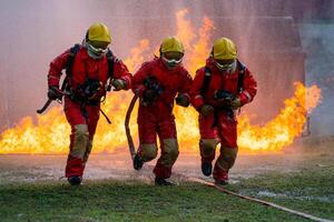 Three firefighters are running through a fire, one of them holding a hose photo