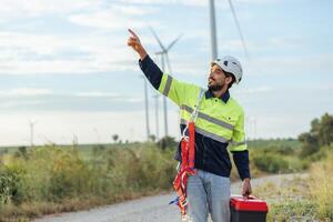 man in a yellow and black safety vest is pointing to a wind turbine photo