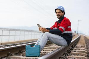 man in a red and blue jacket is sitting on a train track with a tablet in his hand photo