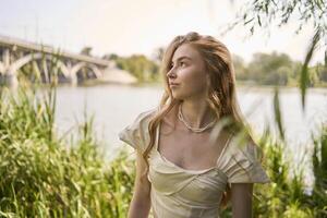 beautiful teenage girl in a silk skirt and a corset in the old money style walks in the park and along the river bank photo
