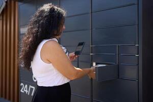 a woman picks up a parcel from a post terminal using a mobile application photo