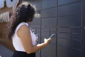 a woman picks up a parcel from a post terminal using a mobile application photo