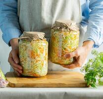 Fermentation preservation Sauerkraut in glass jars in the hands of a woman natural background. Canned food concept. photo