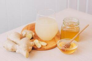 Glass with drink from fresh ginger root, ingredients for its preparation honey lemon kitchen table photo