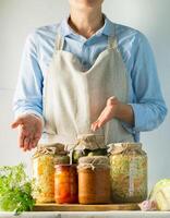 Fermented and canned vegetables various cans stand on the table and a woman cook in an apron. Recycling Autumn Harvest photo