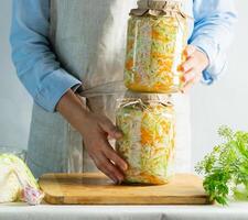 Fermentation preservation Sauerkraut in glass jars in the hands of a woman natural background. Canned food concept. photo