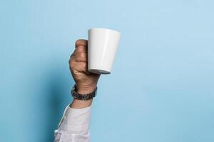 A man holds a cup of coffee or tea drink high in his hand a blue background. Food drink concept. Copy space photo