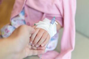 Mother holding child hand with saline IV solution in hospital photo