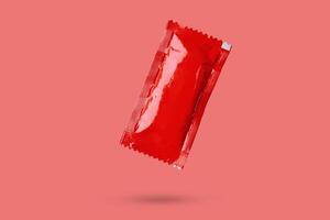 Blank red foil tomato ketchup sauce sachet package float on red background photo