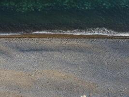 Aerial view from above on azure sea and pebbles beach. Small waves on cristal clear water surface in motion blur. Nature summer ocean sea beach background. Nobody. Holiday, vacation and travel concept photo