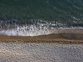 Aerial view from above on azure sea and pebbles beach. Small waves on cristal clear water surface in motion blur. Nature summer ocean sea beach background. Nobody. Holiday, vacation and travel concept photo