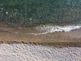 Aerial view from above on calm azure sea and pebbles beach. Small waves on cristal clear water surface in motion blur. Summer ocean sea beach background. Nobody. Holiday, vacation and travel concept photo