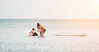 Sea woman and man on sup. Silhouette of happy young woman and man, surfing on SUP board, confident paddling through water surface. Idyllic sunset. Active lifestyle at sea or river. photo