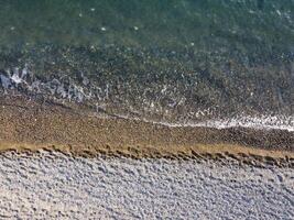 Aerial view from above on azure sea and pebbles beach. Small waves on cristal clear water surface in motion blur. Nature summer ocean sea beach background. Nobody. Holiday, vacation and travel concept photo