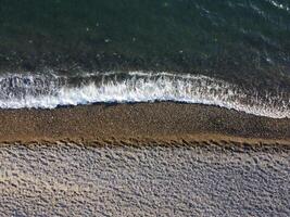 Aerial view from above on azure sea and pebbles beach. Small waves on cristal clear water surface in motion blur. Nature summer ocean sea beach background. Nobody. Holiday, vacation and travel concept photo