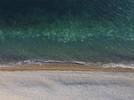 Aerial view from above on azure sea and pebbles beach. Small waves on cristal clear water surface in motion blur. Nature summer ocean sea beach background. Nobody. Holiday, vacation and travel concept photo