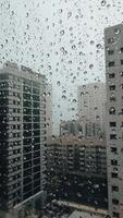 Rain falling on window in skyscraper apartment. Dark and stormy rainy day in big city life. View of dreary Hong Kong cityscape whilst rain drops fall on the window. Abstract somber moody background. video
