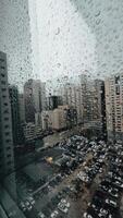 Rain falling on window in skyscraper apartment. Dark and stormy rainy day in big city life. View of dreary Hong Kong cityscape whilst rain drops fall on the window. Abstract somber moody background. video