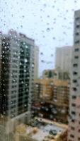 Rain falling on window in skyscraper apartment. Dark and stormy rainy day in big city life. View of dreary Hong Kong cityscape whilst rain drops fall on the window. Abstract somber moody background. video